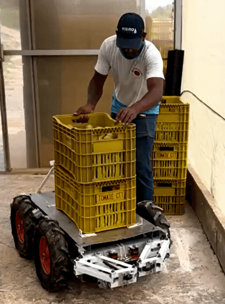 Agrobotz AGR 125,, o robô agricola multitarafe, auxiliando um trabalhador no transporte de caixas de tomate colhido em estufas.